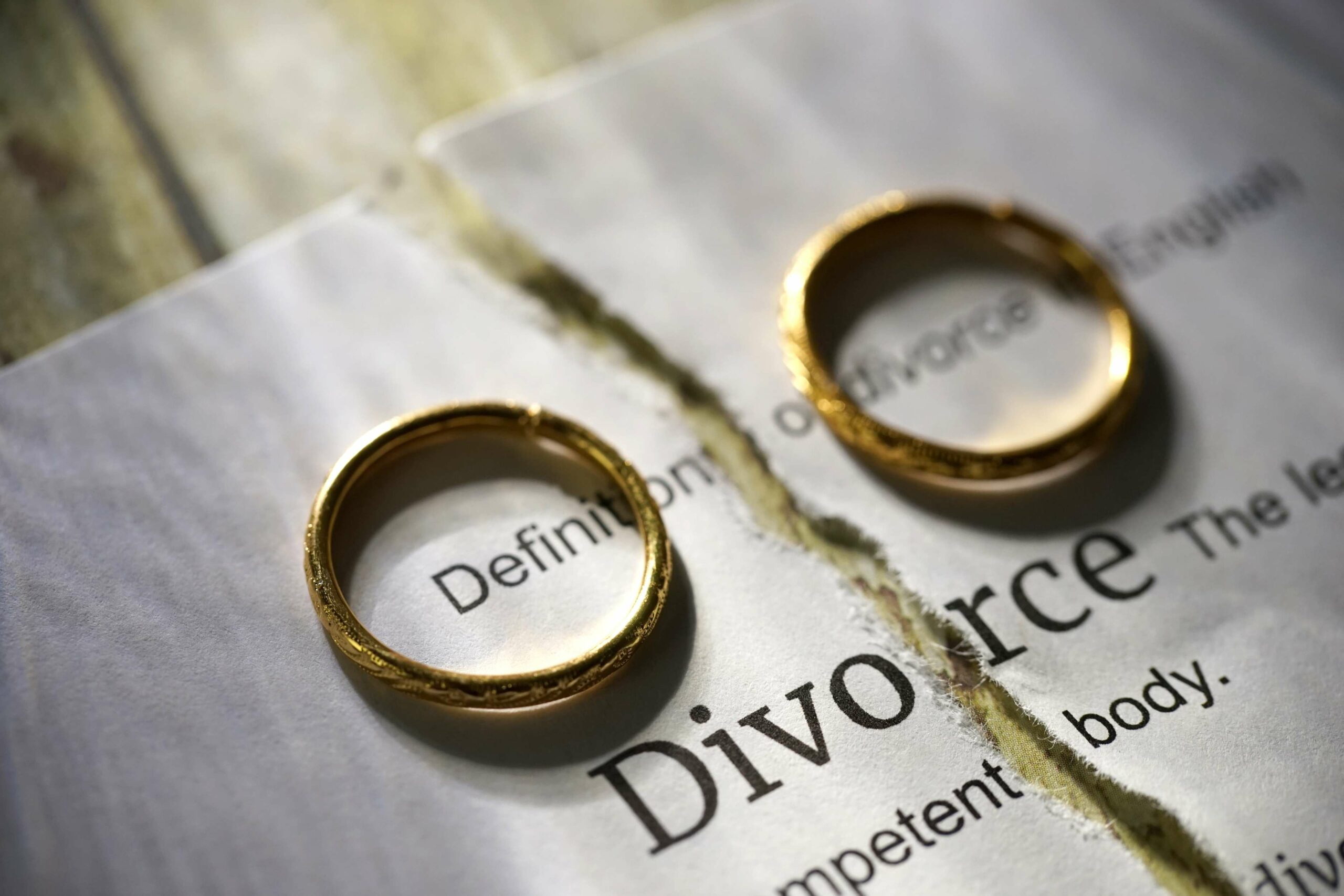 A sheet of paper with 'divorce' written on it is ripped in half. A wedding band is placed on either side of the separated paper.