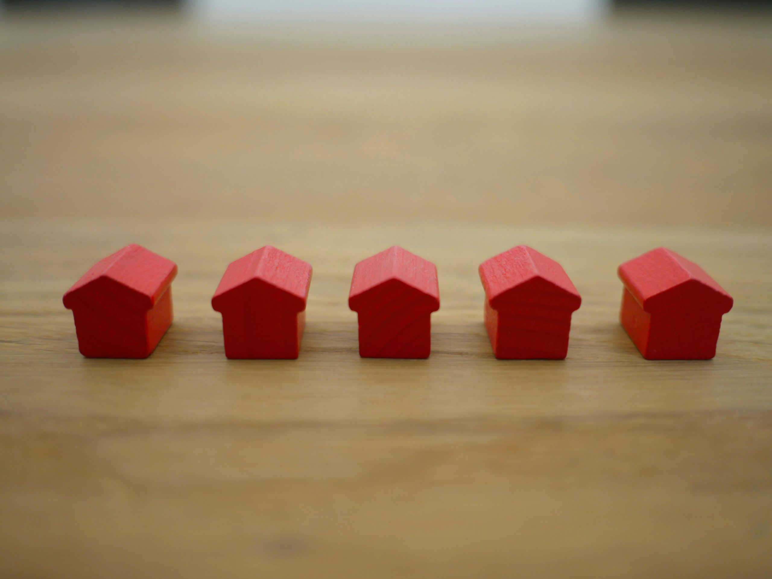 Image shows five small red house figurines lined up on a table to represent Lenders Mortgage Insurance.